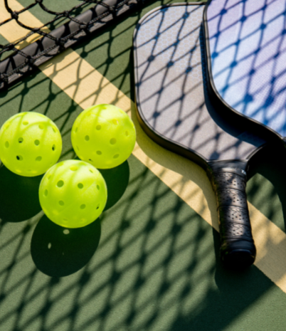 Pickleball paddles and balls placed beside a net.