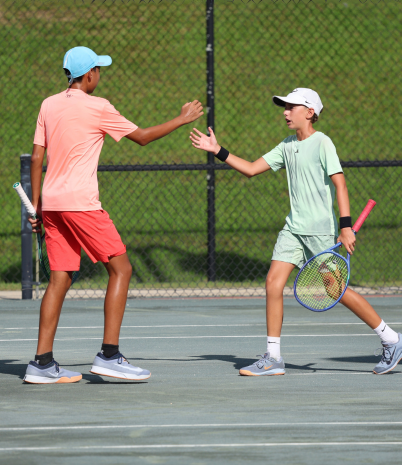 Two jr tennis players high five in celebration on the court